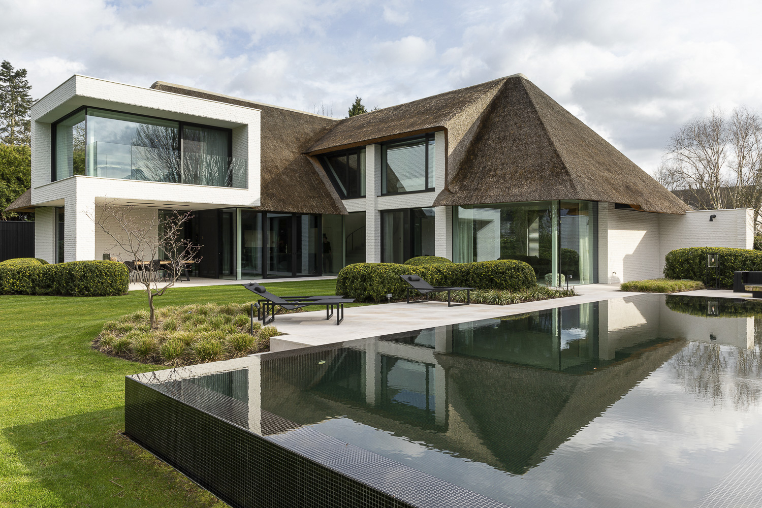 A modern house with a pool and thatched roof.