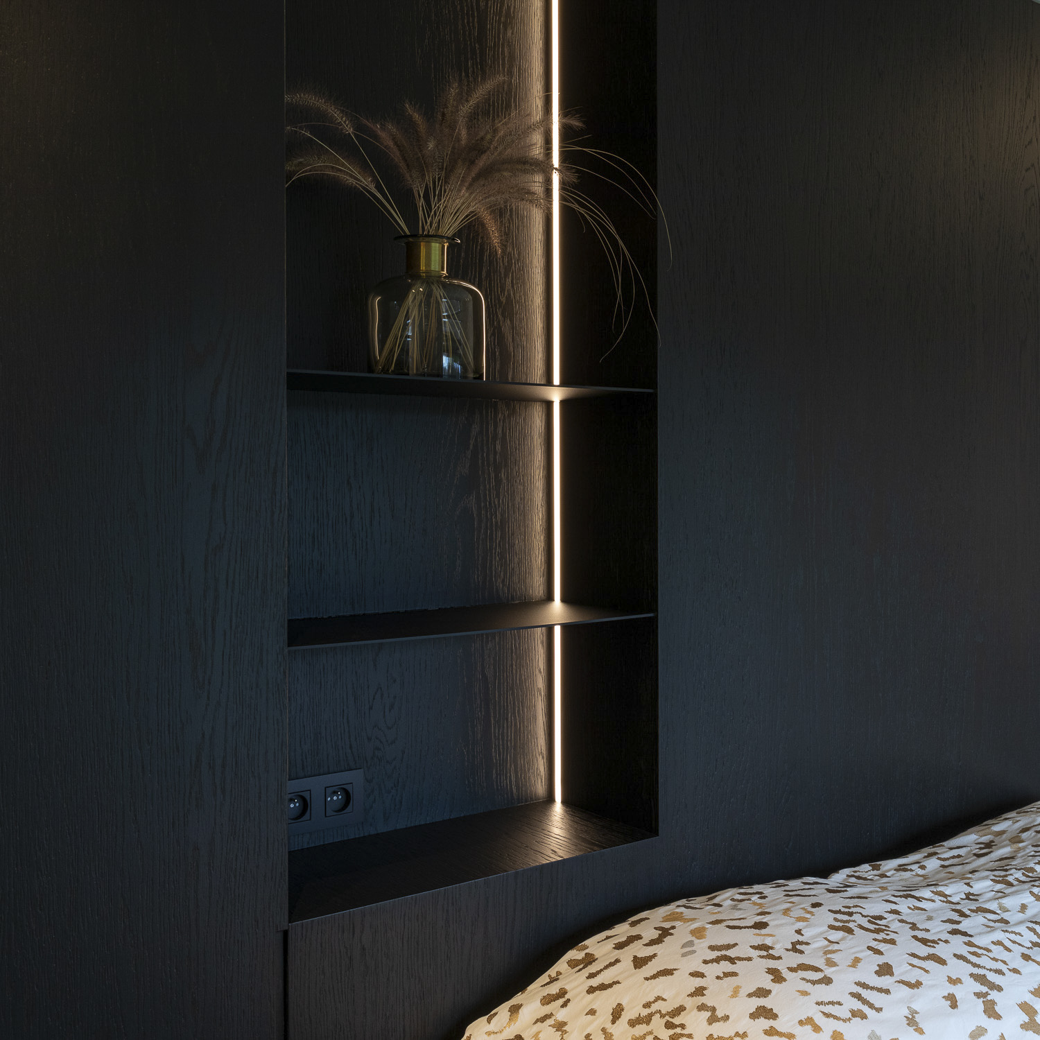 A black bedroom with a bed and a shelf.