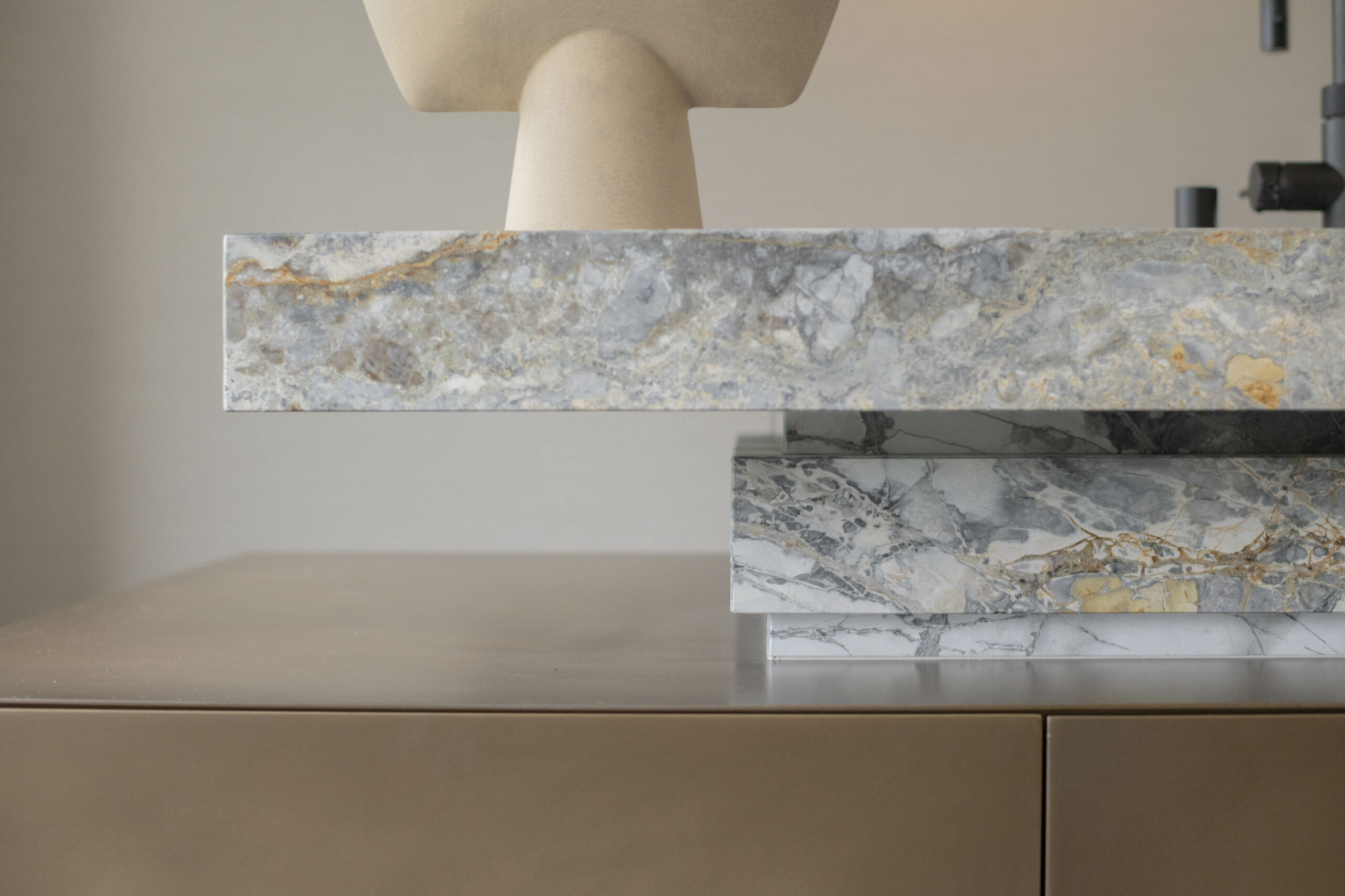 A modern interior with sleek beige surfaces and intricately veined marble slabs, complemented by a sculptural object above.