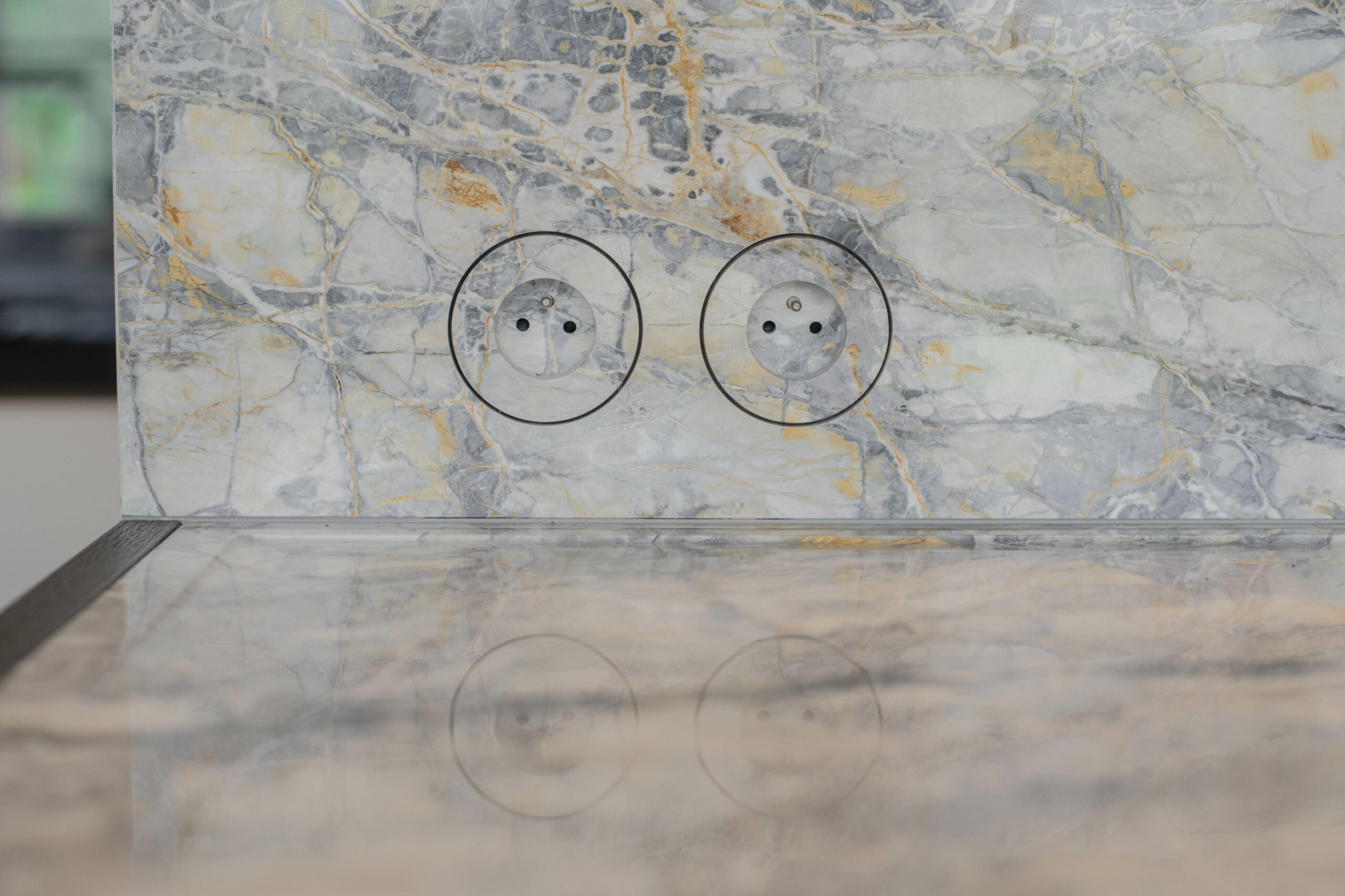 Marble backdrop with two electrical outlets circled, showing intricate patterns in the stone. The polished surface reflects a subtle image below.