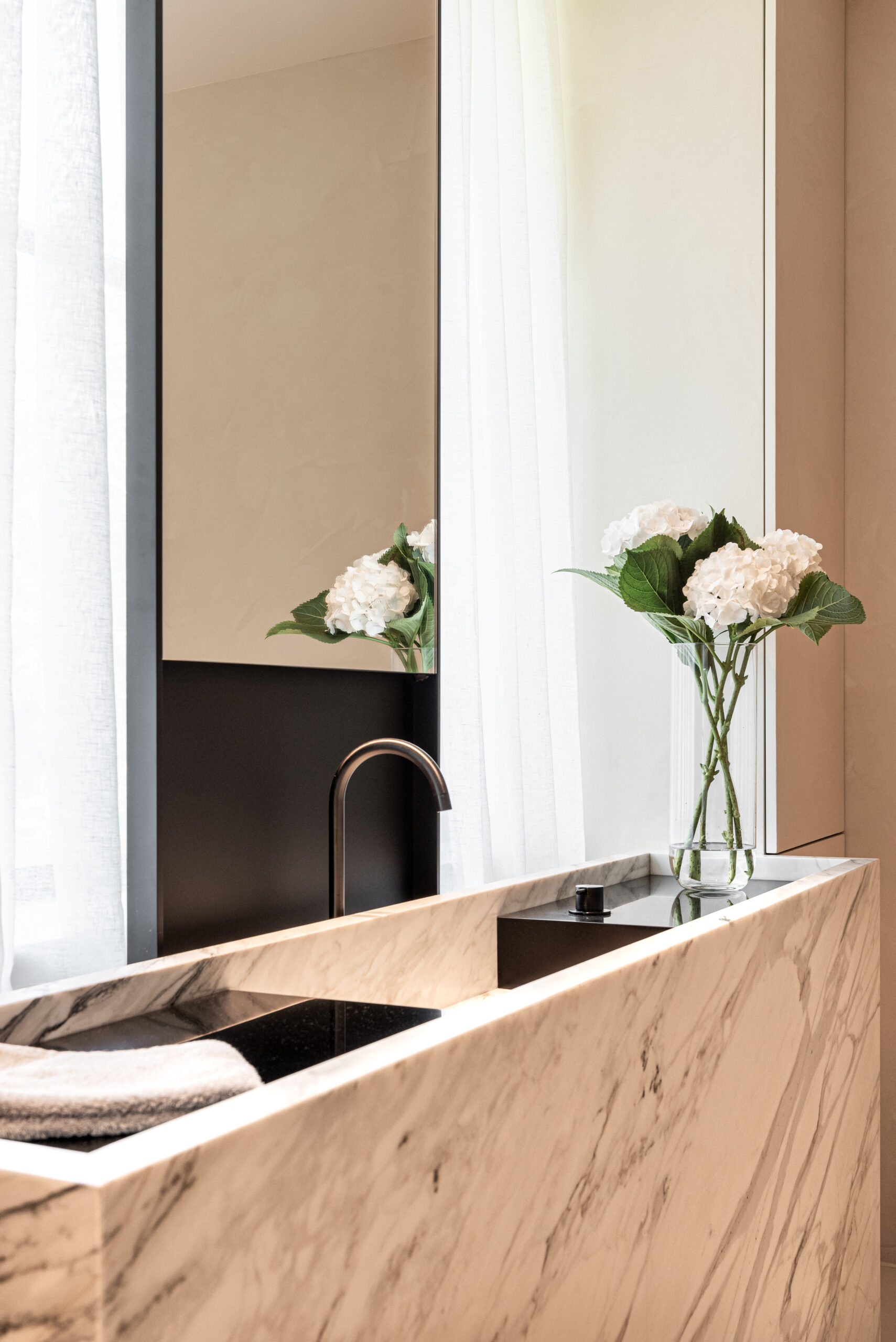 A marble sink complements a vase of fresh hydrangeas in a tranquil bathroom setting.