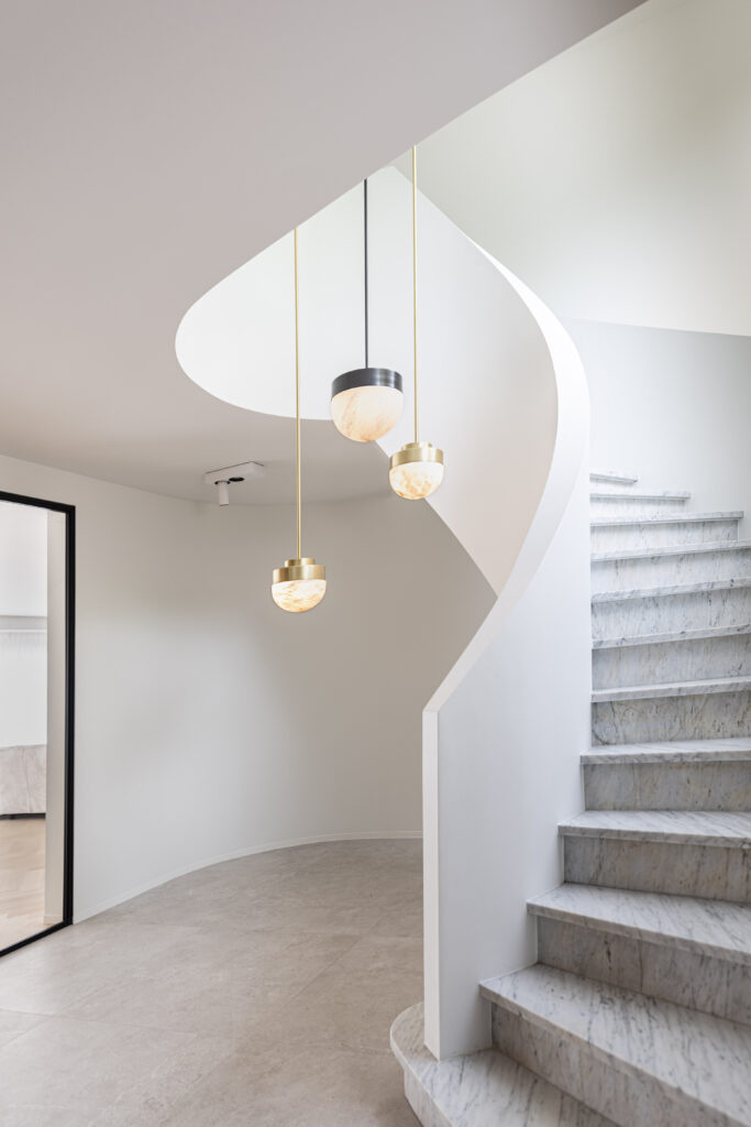 Een moderne binnenruimte met elegante hanglampen die boven een gebogen trap van marmer hangen, aangevuld met een neutraal kleurenpalet.