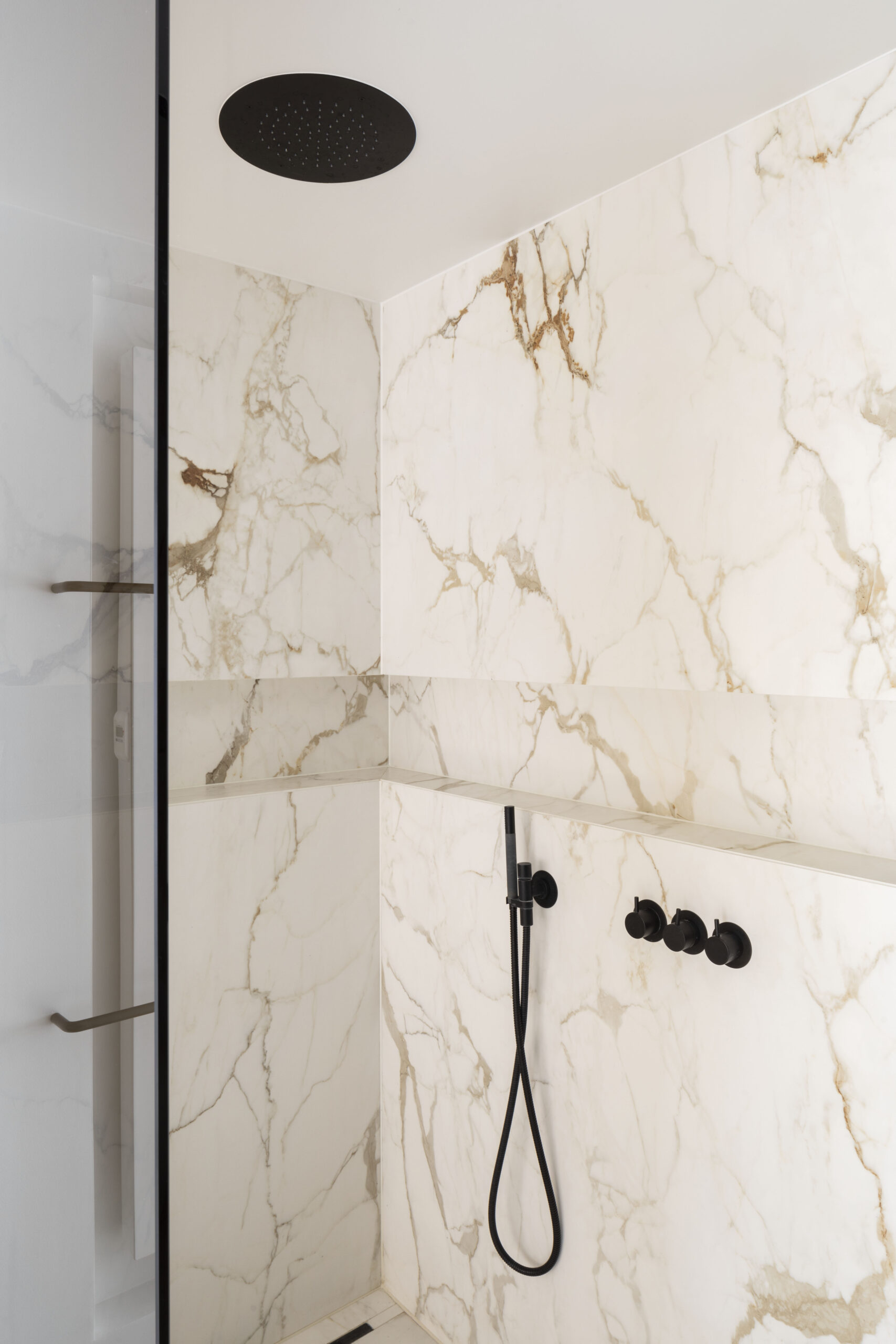 Een elegante douche met marmeren muren en zwarte armaturen.
