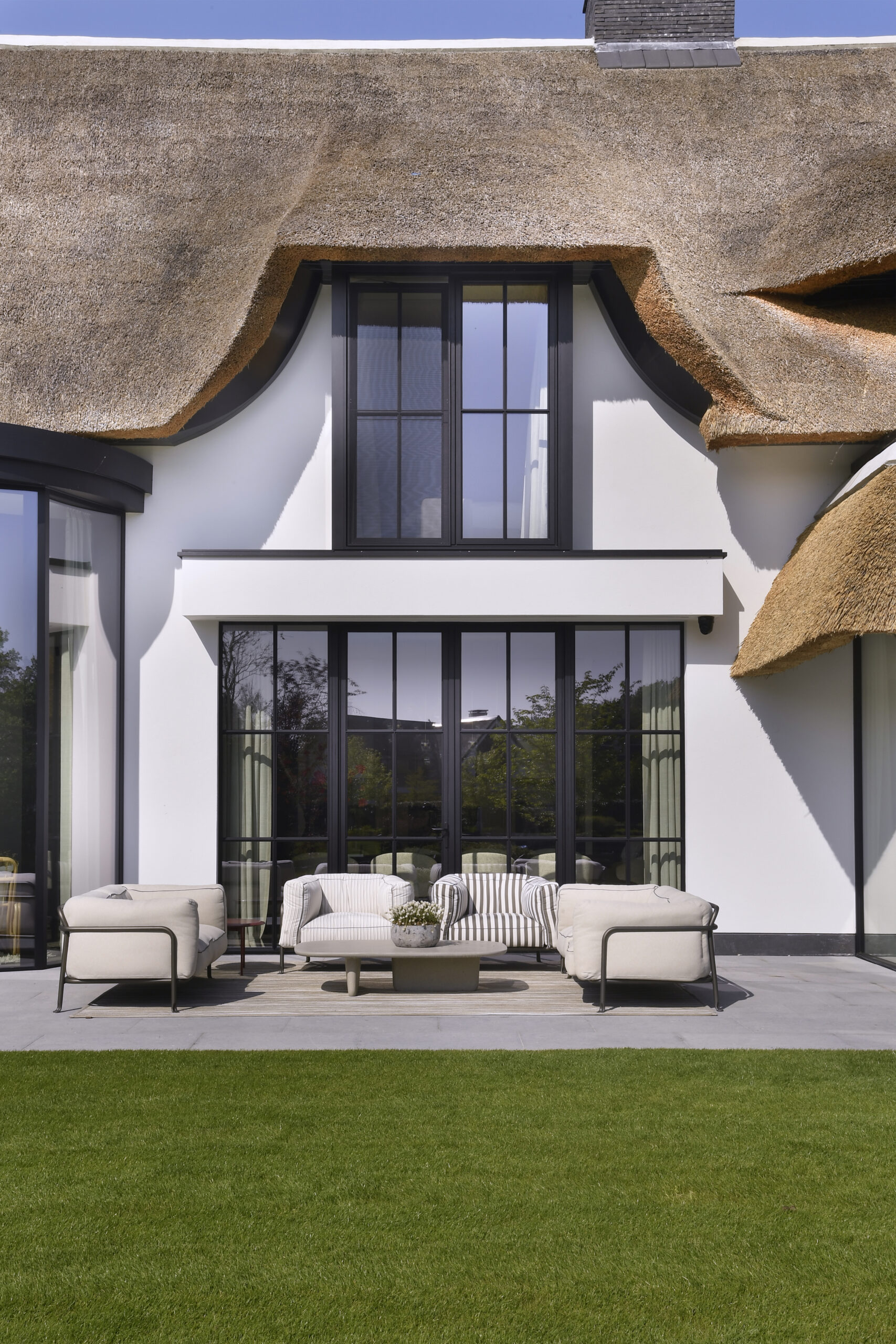Modern house with thatched roof, large windows, and patio seating area.