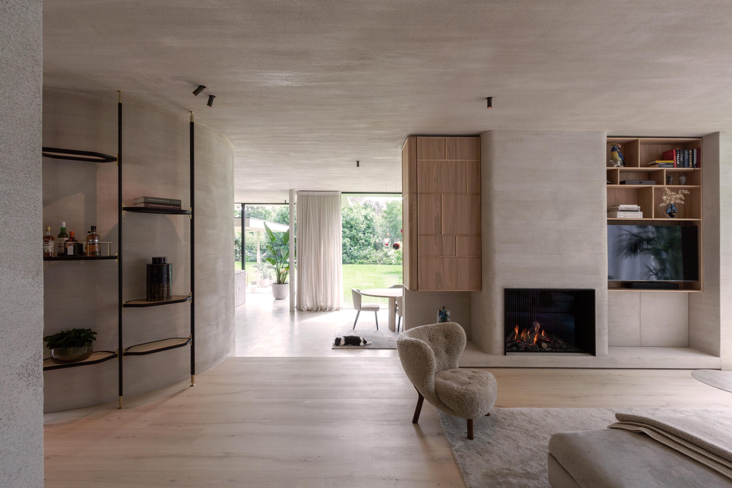Modern living room with muted tones featuring a fireplace, wooden cabinetry, plush seating, and a view to the garden.