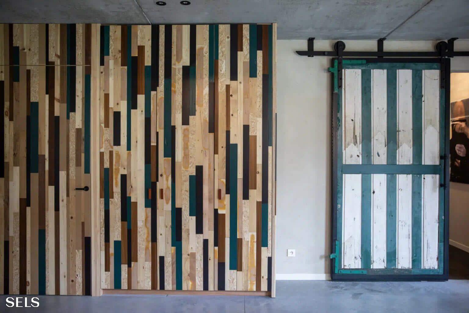 Wand met verticale houten latten in verschillende tinten naast een groen‑witte schuifdeur op een zwart railsysteem.